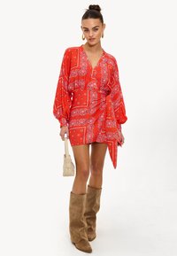 Minivestido con estampado de pañuelo rojo, mangas largas abullonadas, escote en V profundo y dobladillo asimétrico. Combinado con botas altas de tamaño grueso en color beige.