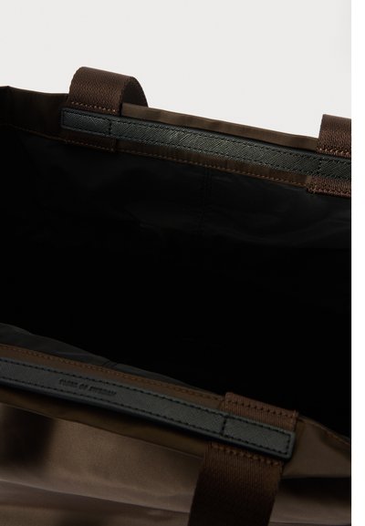 Barna táska sima, fényes felülettel. Fekete belső térrel és dupla szövetfogantyúkkal rendelkezik. Varrott részlet a felső szélén.