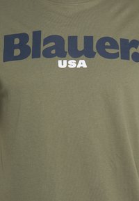 Olivenfarvet t-shirt med stor marineblå "Blauer" tekst og mindre hvid "USA" tekst. Blødt stof med en glat tekstur.