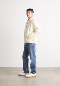 Cremefarvet, fluffy fleecejakke med krave og sidelommer, parret med lyseblå jeans og hvide sneakers med gummisåler.
