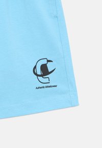 Ανοιχτό μπλε βαμβακερό σορτς με μαύρο λογότυπο και κείμενο "Authentic Athleticwear" στην κάτω αριστερή γωνία. Απλός σχεδιασμός και υφή.