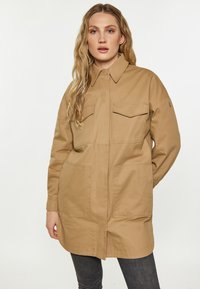 Khaki kurtka robocza z kołnierzykiem, dwoma kieszeniami na piersi i dwoma kieszeniami z przodu. Wykonana z trwałego materiału z lekko luźnym krojem.