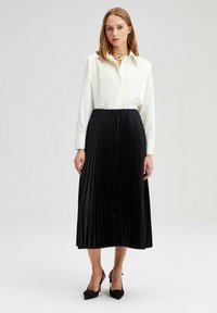 Kemeja putih lengan panjang dipadukan dengan rok midi plissée hitam. Rok tersebut memiliki permukaan tekstur, dilengkapi dengan sepatu hak tinggi hitam.