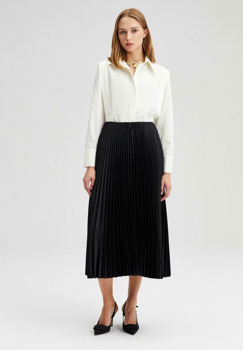 Kemeja putih lengan panjang dipadukan dengan rok midi plissée hitam. Rok tersebut memiliki permukaan tekstur, dilengkapi dengan sepatu hak tinggi hitam.