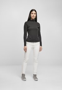 Langermet svart turtleneck med jevn tekstur, kombinert med hvite skinny jeans og grå sneakers. Enkel og tettsittende design.