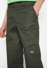 Mörkgröna arbetsbyxor i slitstarkt tyg, med sidofickor och en liten Dickies-logotyp på högra benet.