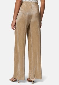 Pantalons en or métallique, avec des plis verticaux, des jambes larges et une taille haute. Tissu texturé avec une finition brillante.