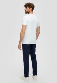 Camiseta blanca de manga corta con cuello redondo, combinada con pantalones azul marino oscuros y zapatillas blancas, vista desde la parte posterior. Textura de algodón suave.