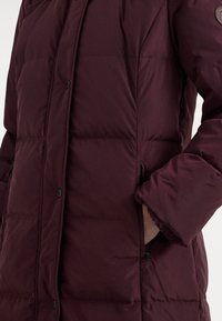 Bordó hřejivá bunda s knoflíkovou přední částí, prošívanou texturou, postranními kapsami a chlupatým okrajem na koncích rukávů.