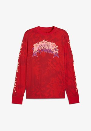 Camiseta de manga larga roja con un gráfico de texto estilo llamas en púrpura y beige en el pecho y texto en cursiva beige a lo largo de ambas mangas.