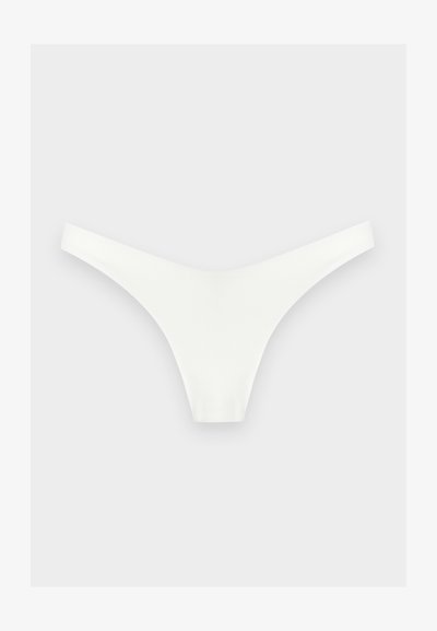 Sous-vêtement blanc sans couture de type string, posé à plat sur un fond gris clair, montrant les bretelles avant et latérales.