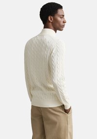 Crew-neck kabelstrikket sweater i off-white, med teksturerede vævede mønstre og ribbet kant. Kombineret med tan løstsiddende bukser.