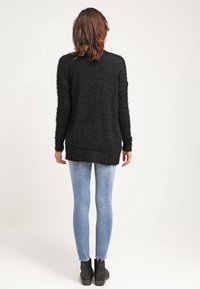 Maglione nero morbido con una vestibilità rilassata, maniche lunghe e orlo arrotondato, abbinato a jeans skinny azzurri e stivaletti alla caviglia.