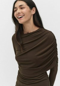 Ruskea, pitkähihainen paita, joka on valmistettu pehmeästä kankaasta. Paidassa on rypytettyjä yksityiskohtia olkapäissä ja vartalon kohdalla, luoden kerroksellista tekstuuria.