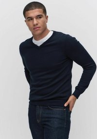 Granatowy sweter w serek wykonany z miękkiego materiału dzianinowego, z długimi rękawami, prążkowanymi mankietami i dopasowanym krojem, zestawiony z ciemnymi dżinsami.