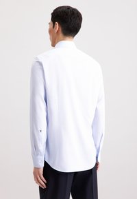 Lichtblauw gestreept overhemd met lange mouwen, knoopmanchetten, een puntige kraag en een gebogen zoom. Glad stoffen textuur.