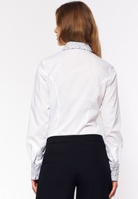 Biała koszula z guzikami, z kołnierzykiem i mankietami w kwiatowy wzór, połączona z czarnymi, dopasowanymi spodniami. Gładka tkanina, dopasowany krój.