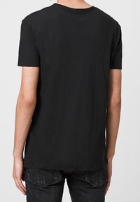 Černé bavlněné tričko s kulatým výstřihem a krátkými rukávy. Tkanina se zdá být jemná a lehká, s volným střihem a mírně zaobleným lemem.