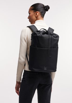 Sac à dos noir à cordon de serrage en tissu durable, avec un dessus resserré, une forme structurée et un détail de logo subtil à l'avant.
