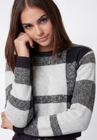 Sort og gråternet sweater med rund hals og ribkanter, der har et blødt, tekstureret strikdesign.