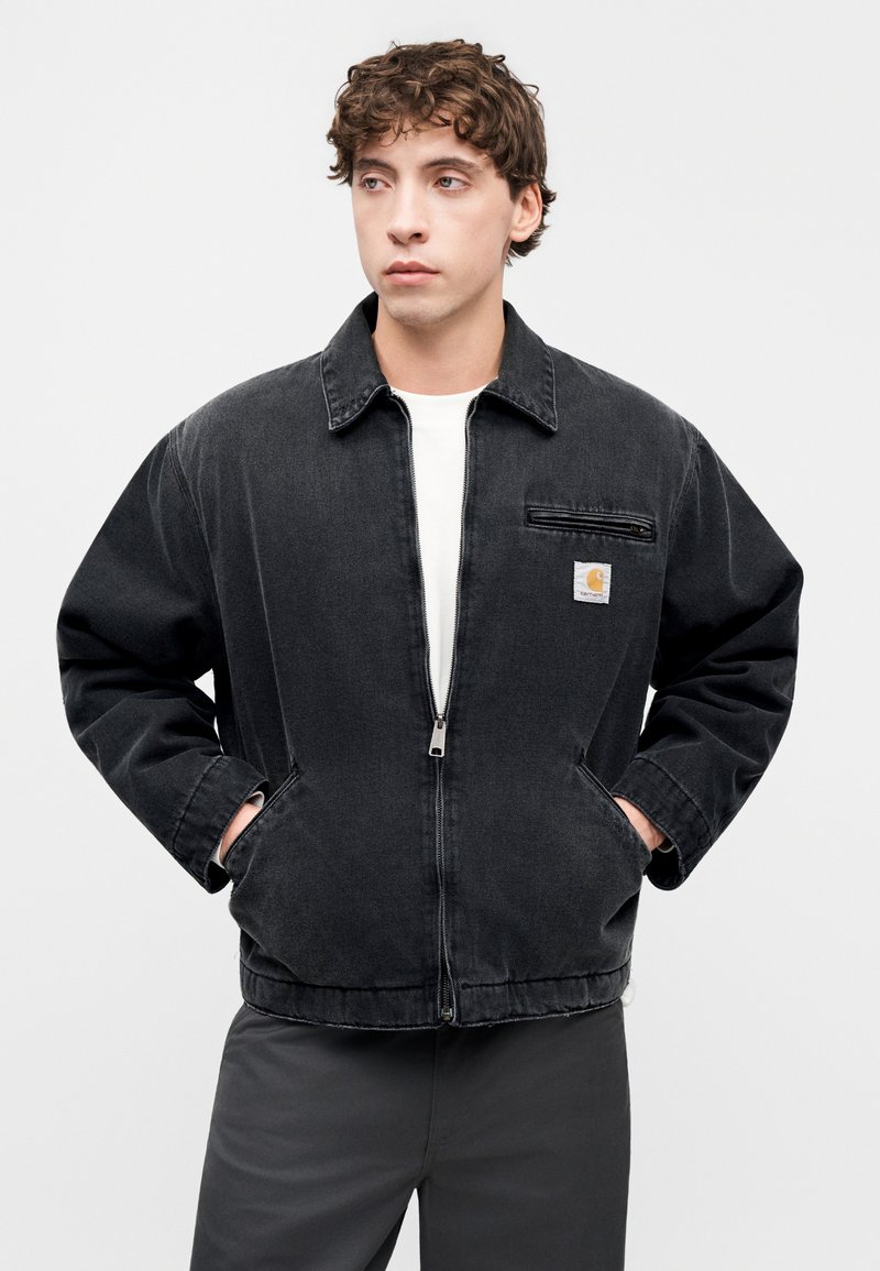 Giacca di jeans nera con colletto, chiusura con zip e due tasche laterali. Presenta una piccola toppa con logo sul petto sinistro e una vestibilità comoda.