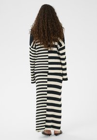 Langes, geripptes Kleid mit schwarzen und cremefarbenen vertikalen Streifen, mit lockerem Schnitt und langen Ärmeln, das unter den Knöcheln endet.