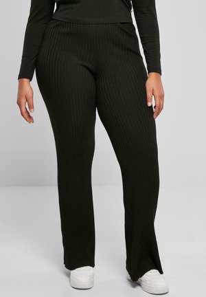 Pantalones de campana negros con relieve y cintura alta, que presentan rayas verticales y una ligera abertura en el dobladillo, combinados con zapatillas blancas.