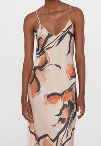 Robe en satin à fleurs avec un décolleté en V, des bretelles fines, et une base beige doux ornée de motifs floraux abstraits noirs et orange.