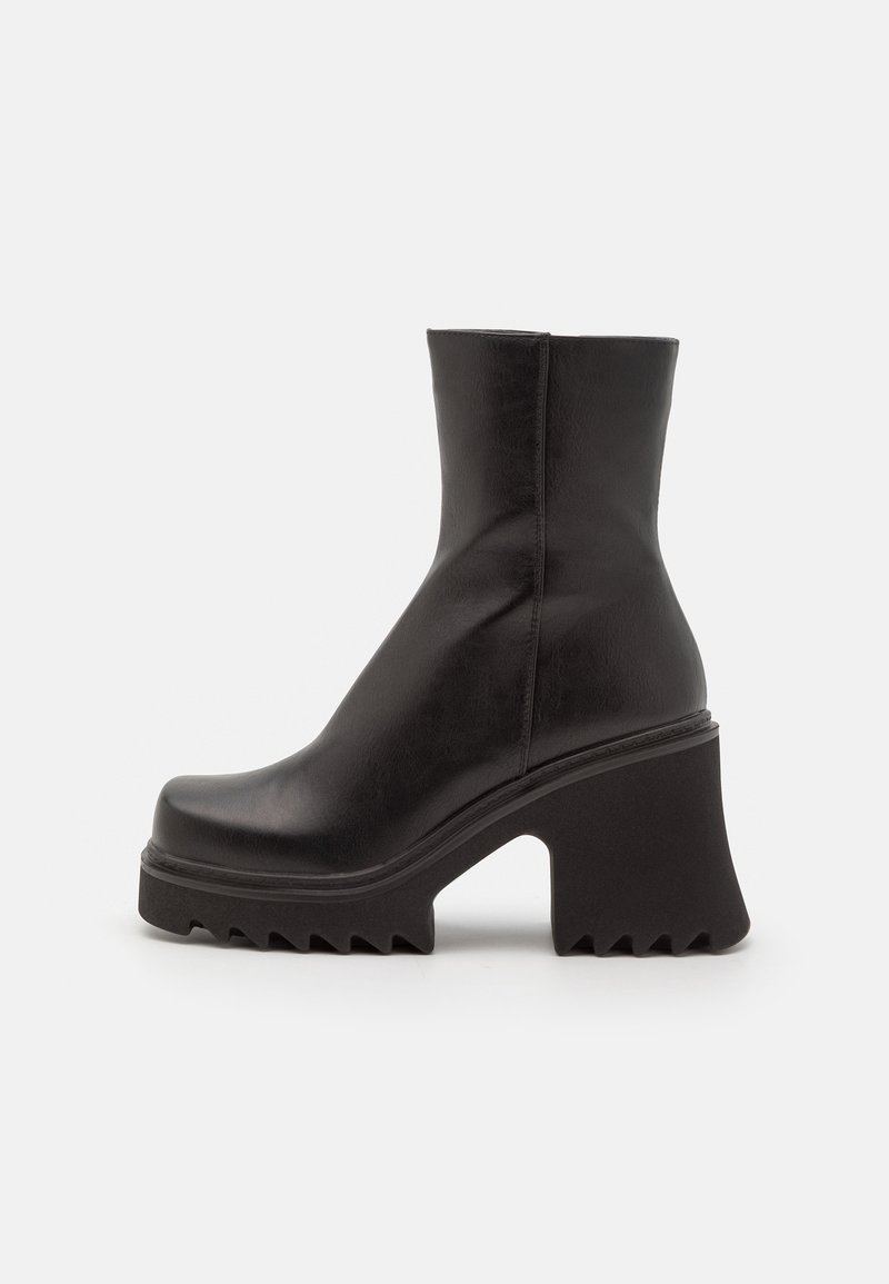 Botte en cuir noire mi-mollet avec talon bloc épais et semelle épaisse à crampons, vue de profil sur fond clair.