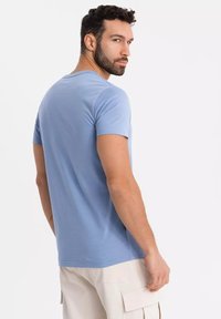T-shirt azzurro a maniche corte in tessuto morbido, con collo a giro e taglio dritto. Il modello indossa pantaloni cargo chiari.