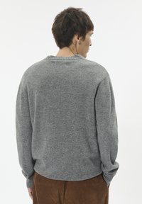 Pulover gri tricotat cu gât rotund și mâneci lungi. Țesătura are o textură moale. Purtați cu pantaloni din bumbac cu fante din catifea maro.