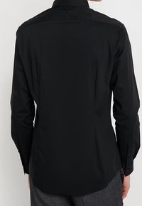 Zwart lang uitshirt gemaakt van gladde stof, met een standaard kraag, knoopmanchetten en een gebogen zoom. Eenvoudig en slim-fit ontwerp.