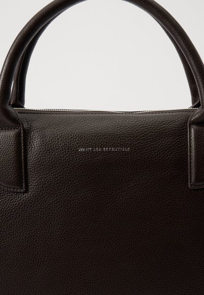 Brown leather handbag with a textured surface. Features sturdy handles and silver embossed text reading “WANT LES ESSENTIELS.”