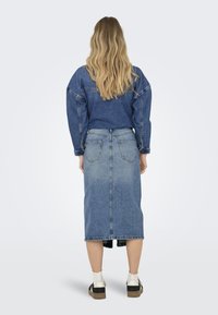 Denim jakna z oversized krojem, v kombinaciji z visokim denim krilom. Obe stvari sta srednje modri z malo zbledelim videzom.
