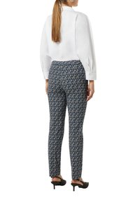 Witte blouse met lange mouwen, gecombineerd met gestreepte marineblauwe broek met geometrische ontwerpen. Model draagt zwarte hoge muiltjes.