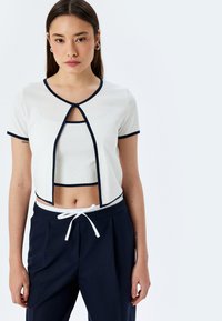 Witte geribde top met korte mouwen en marineblauw accent, gecombineerd met hoge marineblauwe broeken met een witte trekkoord.