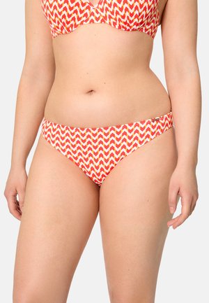 Mujer con bikini de patrón chevron en rojo, naranja y blanco, con la parte superior a juego, contra un fondo claro y simple.