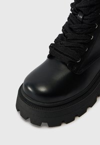 Czarne, masywne botki na platformie, wykonane z gładkiej skóry, z textured czarnym sznurowaniem, okrągłym noskiem i gumową podeszwą z głębokim bieżnikiem.