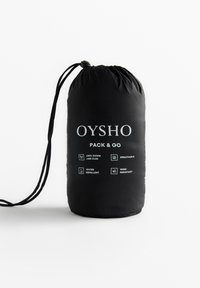 Črn zložljiv nahrbtnik z vrvico za zapiranje. Vsebuje belo besedilo, vključno z "OYSHO", ter simbole za 100% puhovino, zračnost, vodoodpornost in odpornost na veter.