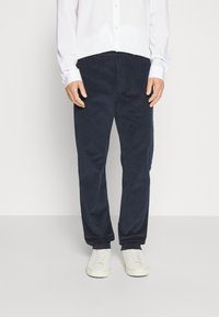 Pantaloni in velluto a coste blu navy con una vestibilità dritta, dotati di tasche frontali e abbinati a sneakers bianche. Texture liscia, vestibilità casual.