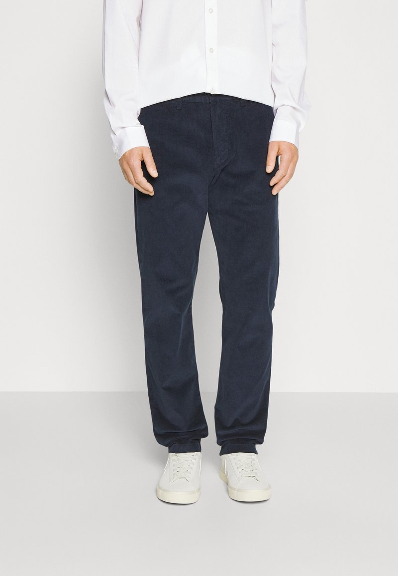 Pantaloni in velluto a coste blu navy con una vestibilità dritta, dotati di tasche frontali e abbinati a sneakers bianche. Texture liscia, vestibilità casual.