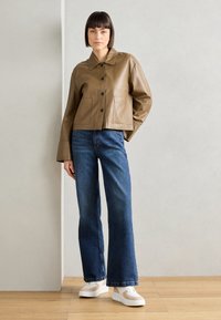 Veste cropped en cuir marron avec un col, ornée de boutons noirs et de deux poches avant, associée à un jean en denim bleu à jambes larges.