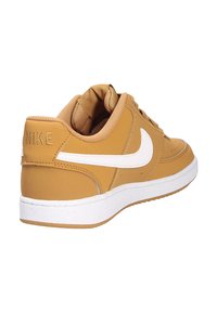 Nike sneakers i tan læder med hvid swoosh, polstret tunge og struktureret gummisål. Subtile syninger på overdelen.