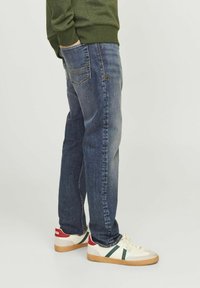 Vaqueros de denim azul claro con corte recto, cinco bolsillos y un sutil detalle de costura; combinados con zapatillas blancas de caña baja con acentos verdes.