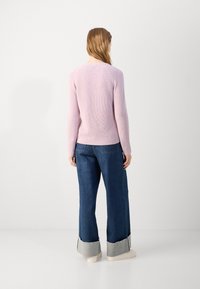 Pulover tricotat roz deschis cu mâneci raglan, cu un finisaj texturat. Asortat cu blugi largi de culoare albastră, având manșete gri contrastante.