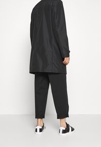 Black long coat, black trousers with rolled cuffs, and black sneakers with white accents. Smooth texture, minimal design, and no visible patterns.