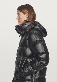 Black puffer jacket with a shiny finish, featuring a hood, high collar, and visible stitching. Two side pockets are integrated into the design.