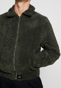 Groene fleecejas met ritssluiting, voorzien van een kraag, geribbelde zoom en zijzakken, met een zachte, getextureerde stof.