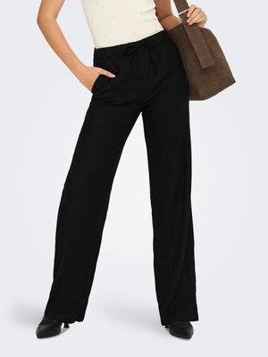 Woman wearing black wide-leg pants with elastic waist and drawstring, holding a brown suede handbag on her shoulder.