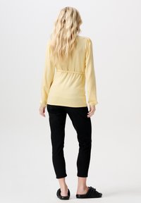 Geel langemouwen top met een getailleerde taille, gecombineerd met zwarte, strakke broeken en zwarte instapsandalen; gladde stof en eenvoudig ontwerp.
